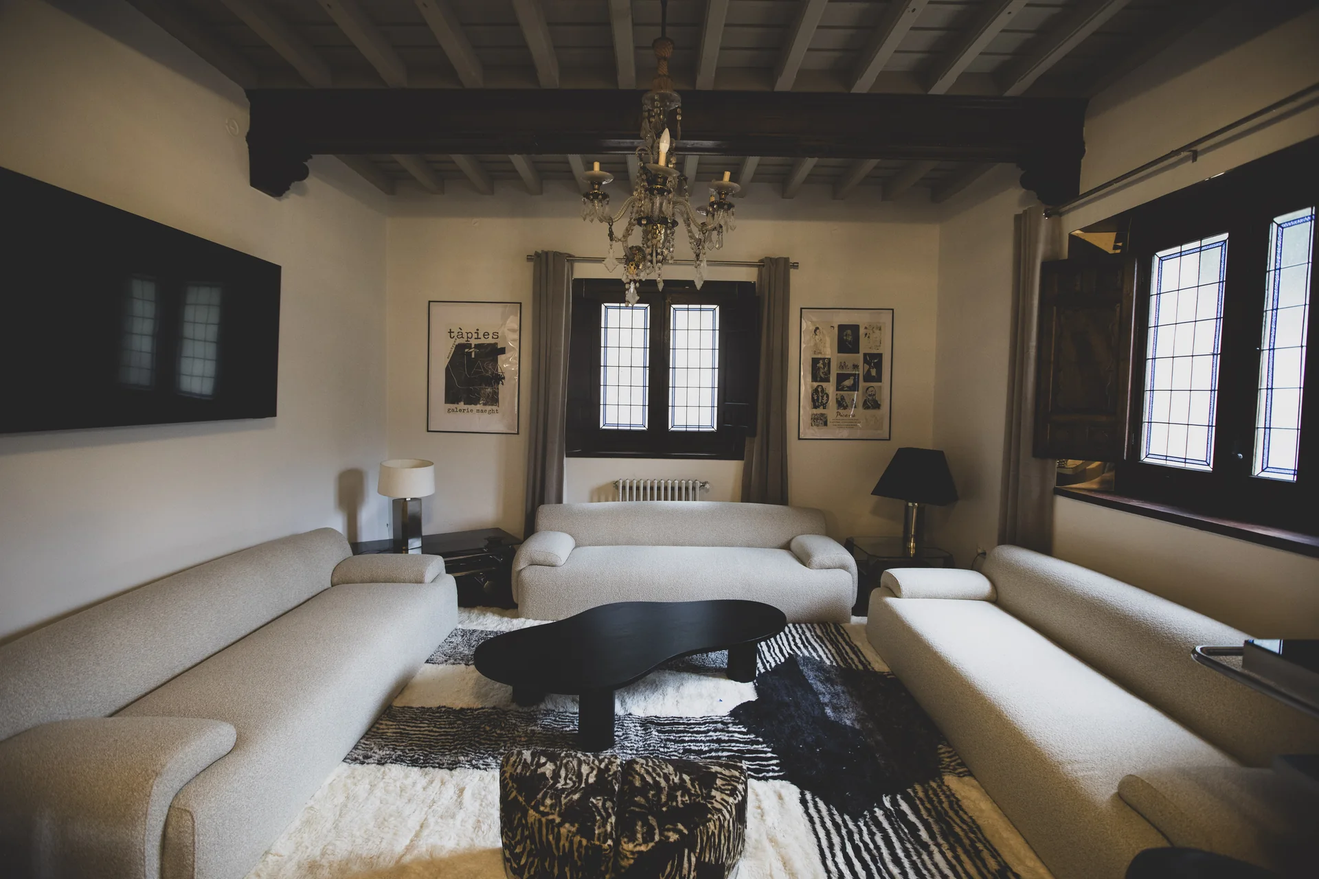 Salón con sofás claros, mesa baja oscura y ventanas de madera.