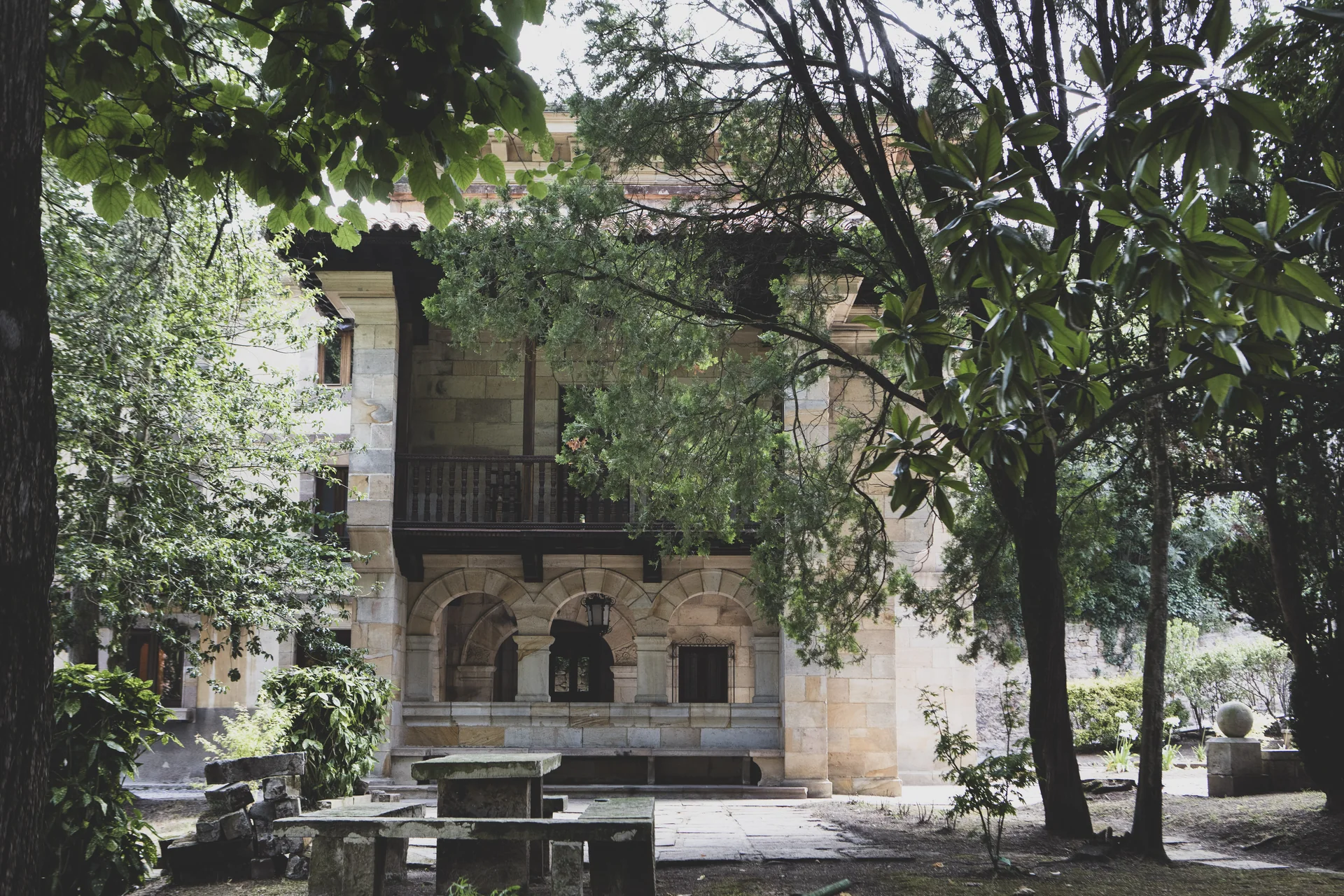 El Palacio visto entre los árboles, con una mesa de piedra en el jardín.