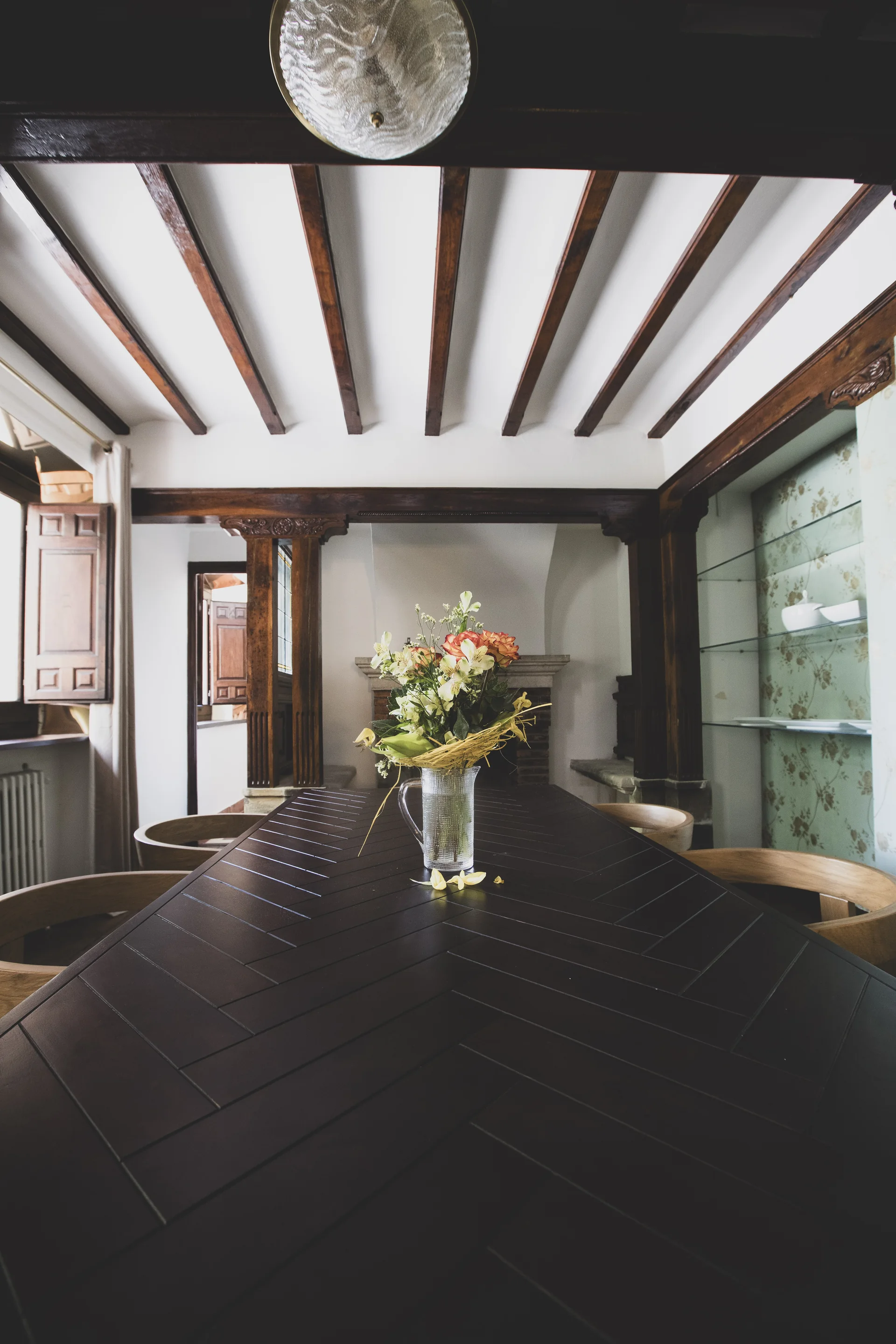 Mesa de comedor de madera con flores y sillas bajo un techo de vigas.